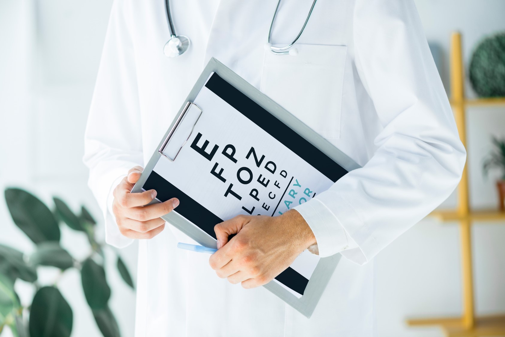 Okulista w białym kitlu trzyma w rękach tablicę do badania wzroku.