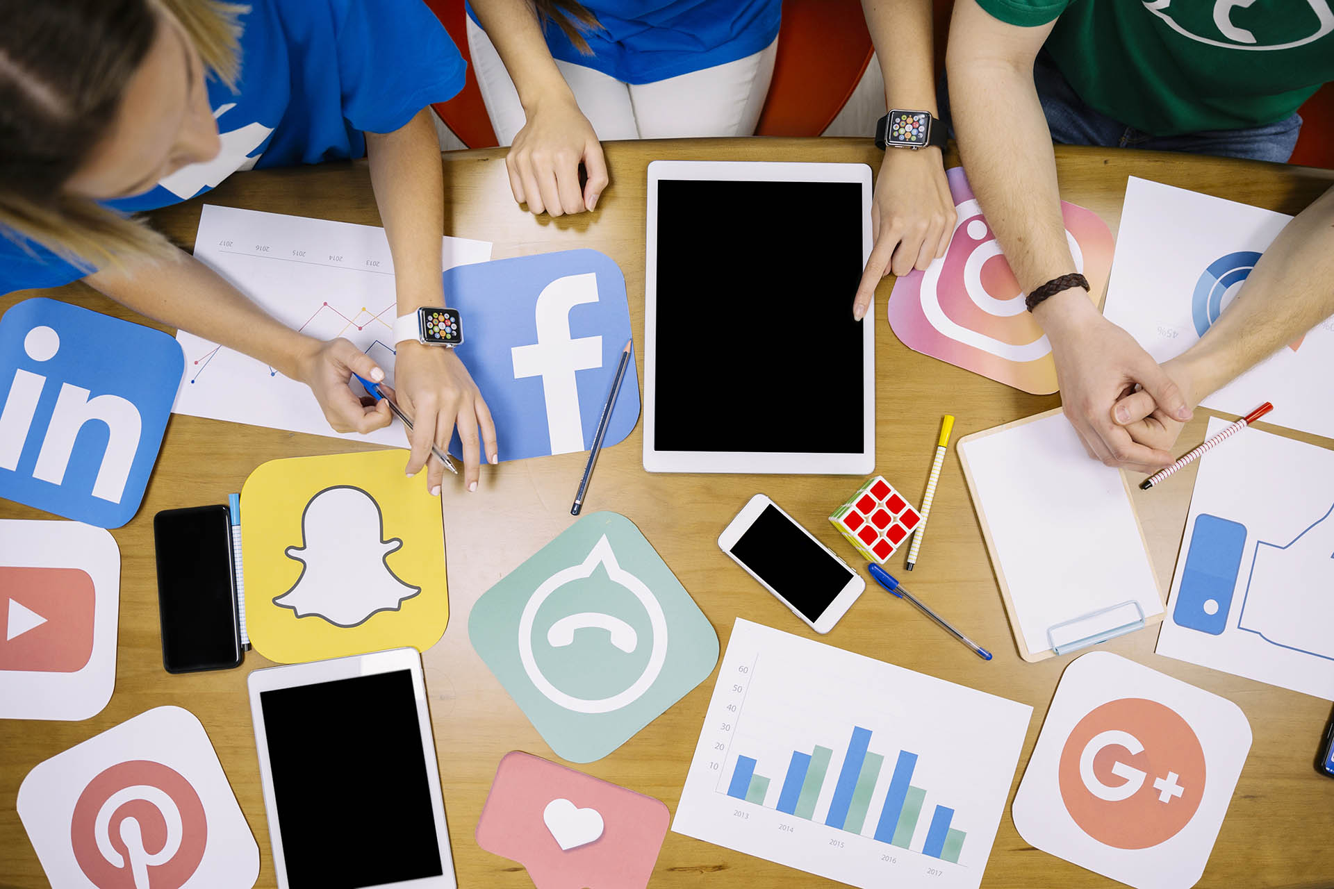widok z góry na stół, przy którym siedzą ludzie. Na stole widać tablet oraz kartki z logotypami najpopularniejszych serwisów społecznościowych